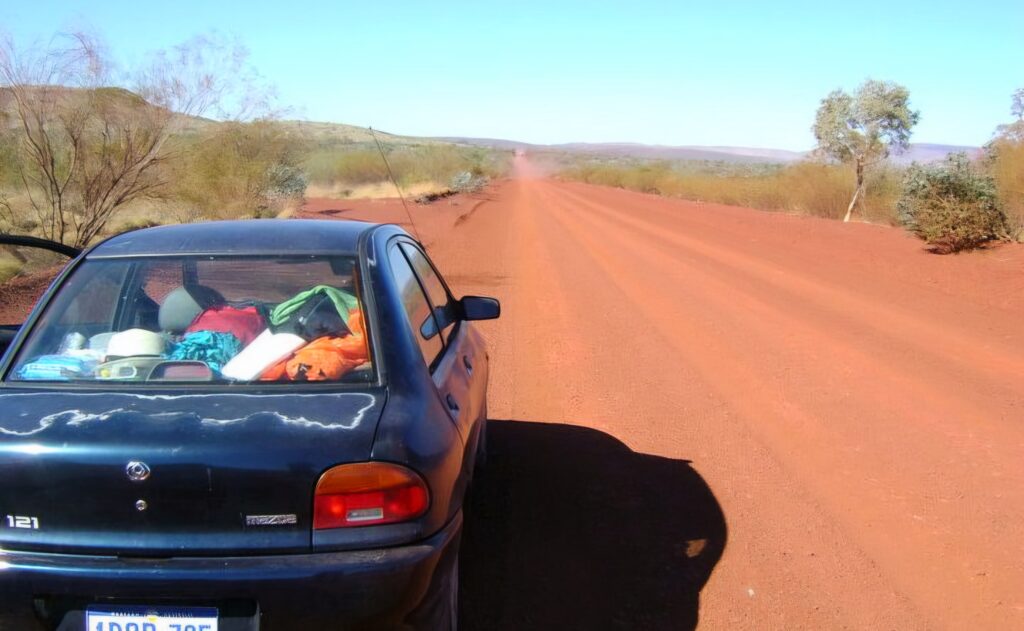 A hatchback car parked on a red dirt road in the Australian outback