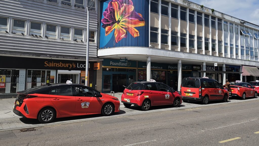 A line of red taxis outside shops in Exeter City