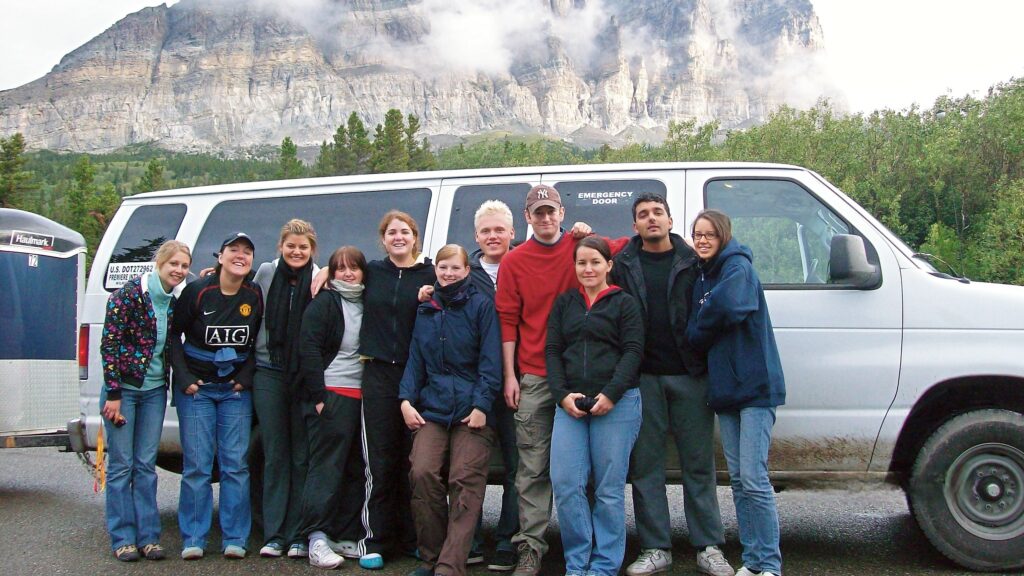 A group of people on an organised tour stood outside of a white van in front of a mountain