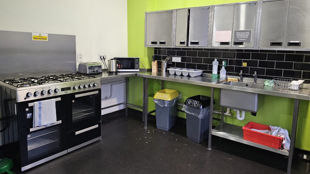 Hostel kitchen consisting of a cooker, metal cupboards and a sink