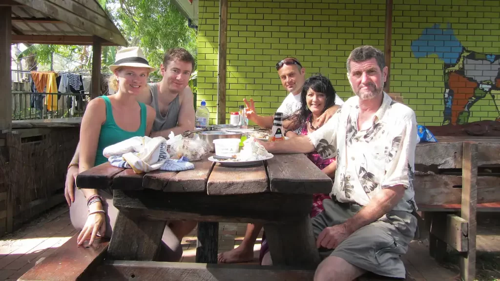 Five people both young and old hanging out together on a picnic bench in a hostel