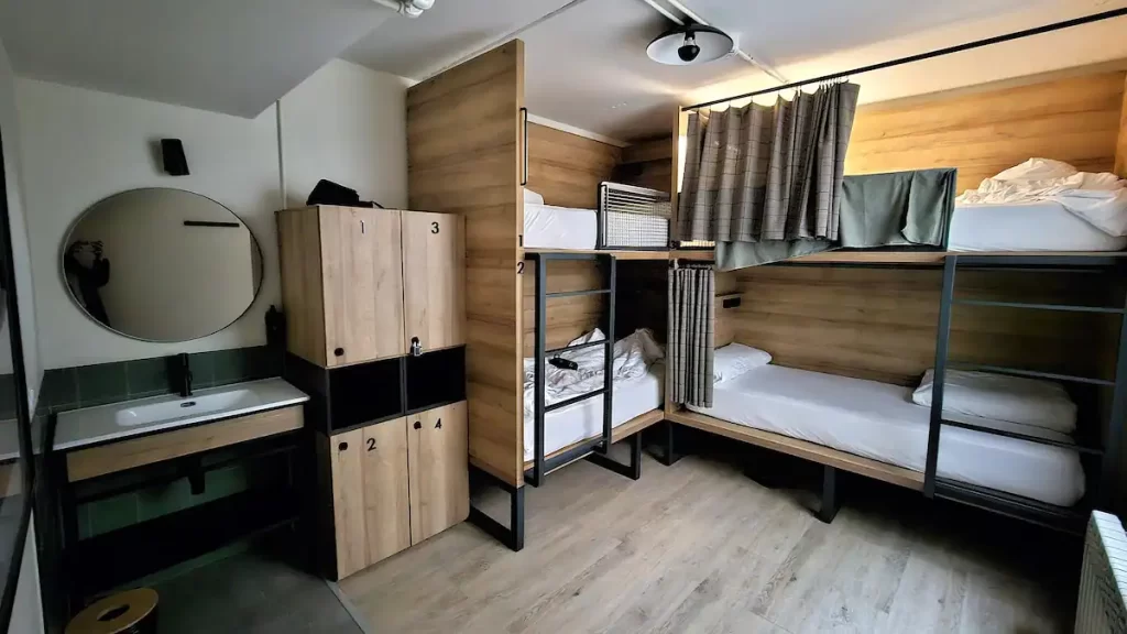A clean modern looking hostel dorm room with two sets of bunk beds, four lockers and a sink.