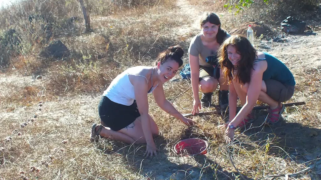 Three young woman bend over making a pitfall trap