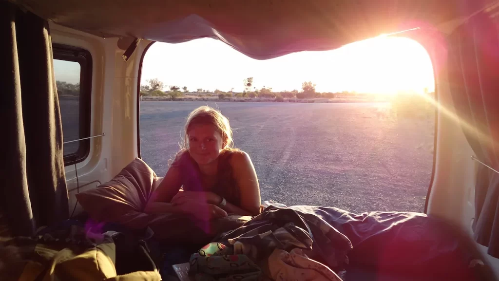 Sue (the founder of the Practical Passport) in the back of a campervan with a sunset behind her