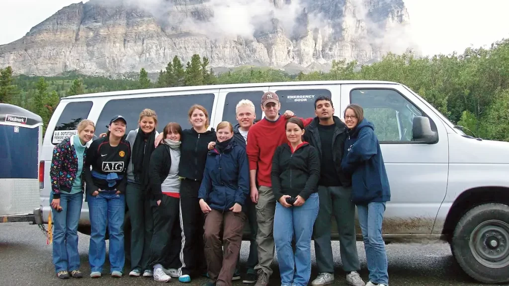 A group of people on an organised tour stood outside of a white van in front of a mountain