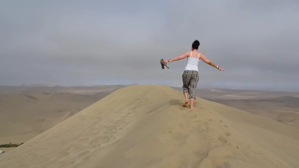 Woman walking barefoot on top of sand dunes