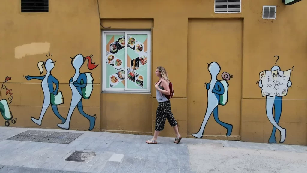Woman walking in front of a wall with graffiti depicting people walking
