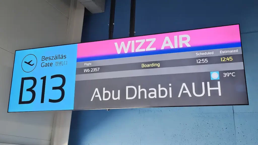 An airport gate sign showing Wizz Air flight to Abu Dhabi