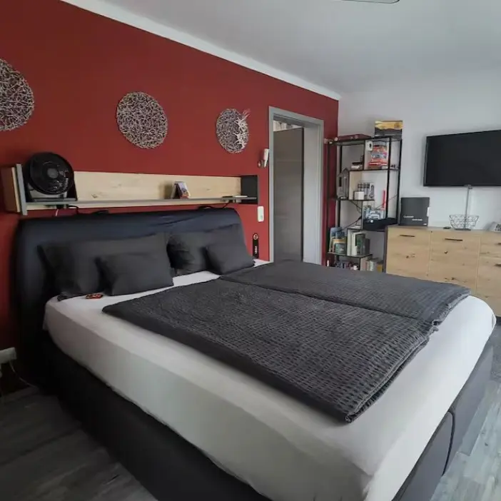 A double Airbnb bedroom with one red wall and wooden and metal decor