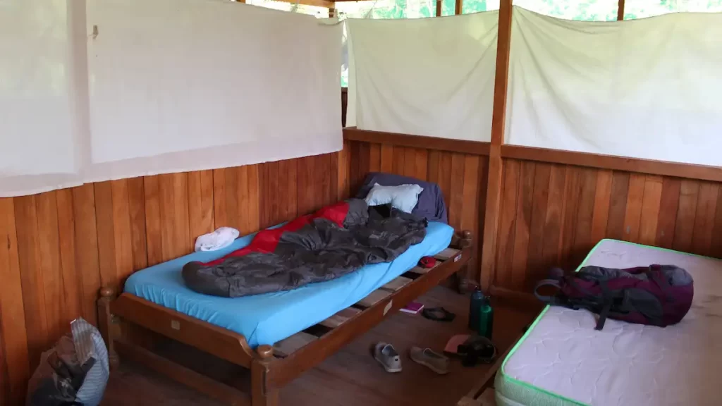 A basic wooden bed in a hut with a sleeping bag on it