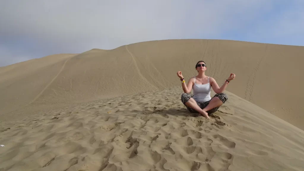 A woman sat crossed legged meditating on top of a sand dune in a desert