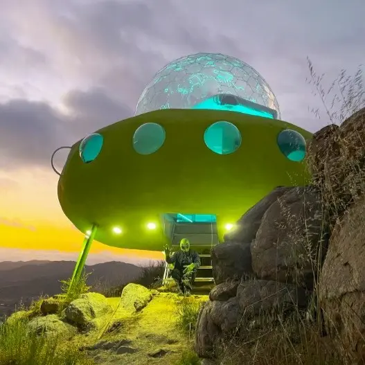 The exterior of an Airbnb shaped like a UFO with an alien sat at the base of the steps