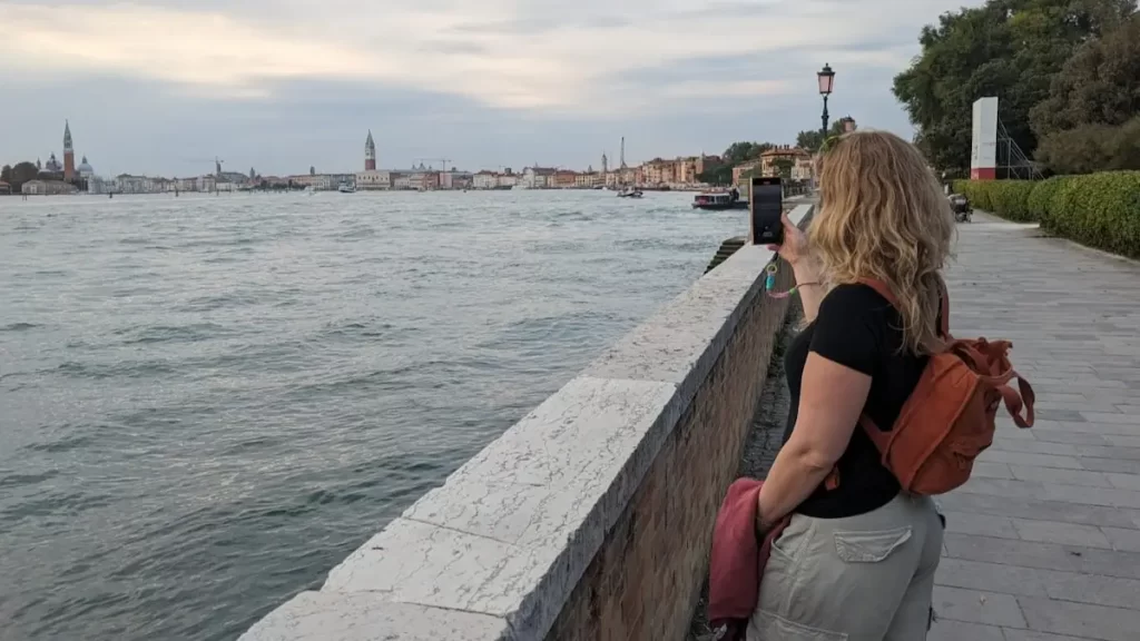 A woman taking a photo of the Venician skyline using a smartphone which has a wrist strap attached