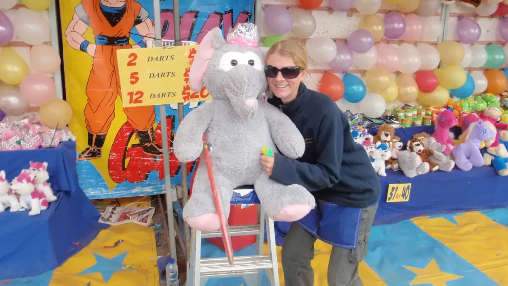 Girl hugging a giant elephant teddy stood in front of a wall of balloons which is a burst-a-balloon stall