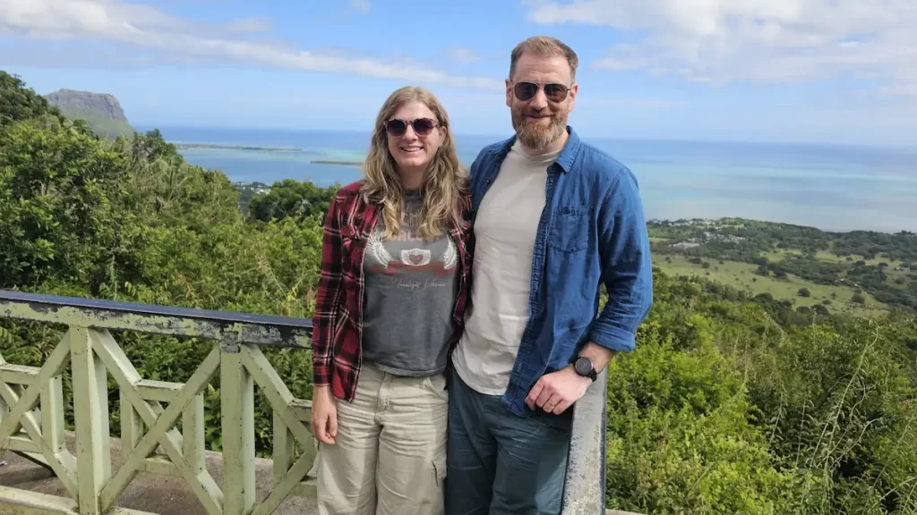 Sue and Jon with arms around each other overlooking the ocean in Mauritius on a sunny day with blue sky