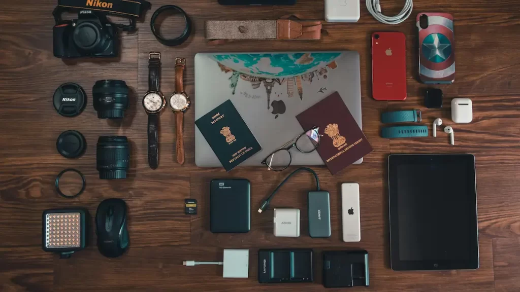 A flat lay view of various technology including a DSLR camera, laptop, tablet, external hard drives, smartphones and memory cards