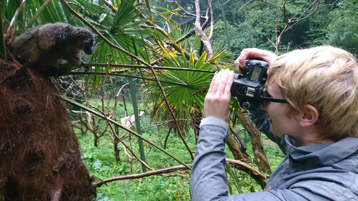Blonde woman with short hair taking a photo of a lemur using a DSLR camera