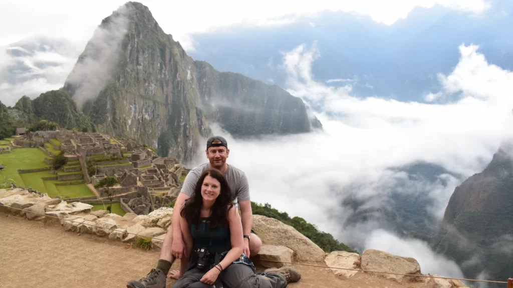 Sue and Jon sat in front of Machu Picchu with mountains and clouds in the background