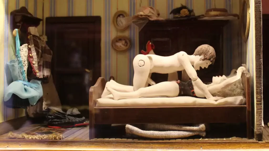 Two miniature figures posed in the missionary position inside a dolls house