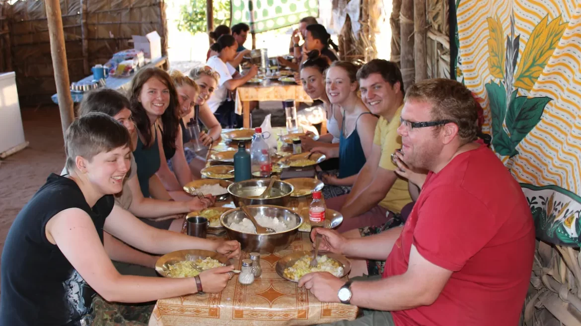 Group of young adults around a long rectangle table in a dusty camp setting