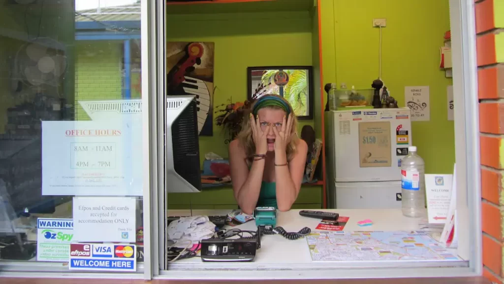 Sue (founder of The Practical Passport) sat behind a hostel reception desk with her hands covering her face pulling a mock screaming expression