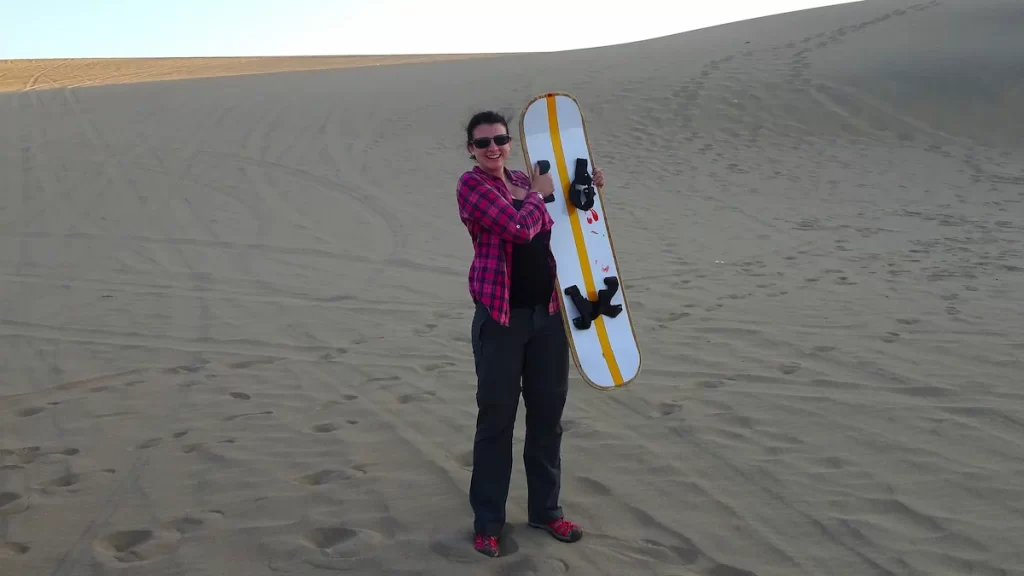 Woman smiling and holding a sandboard in the middle of a desert
