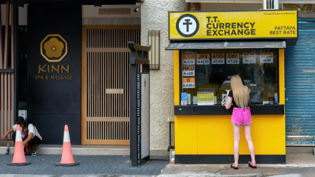 Blonde woman stood at a yellow currency exchange booth on a street