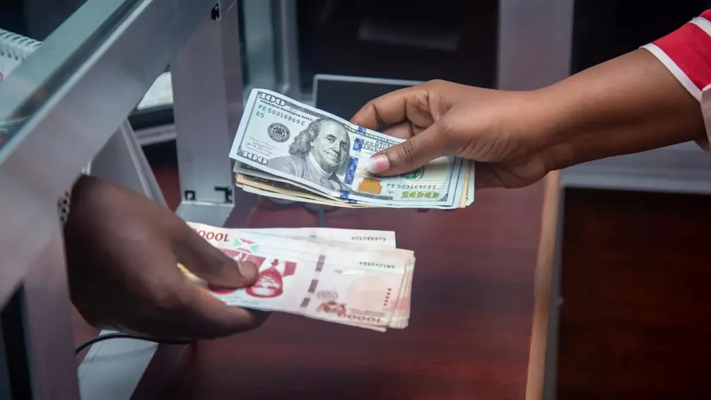 Close up of two different people's hands holding notes of different currencies and exchanging it though a bank hatch
