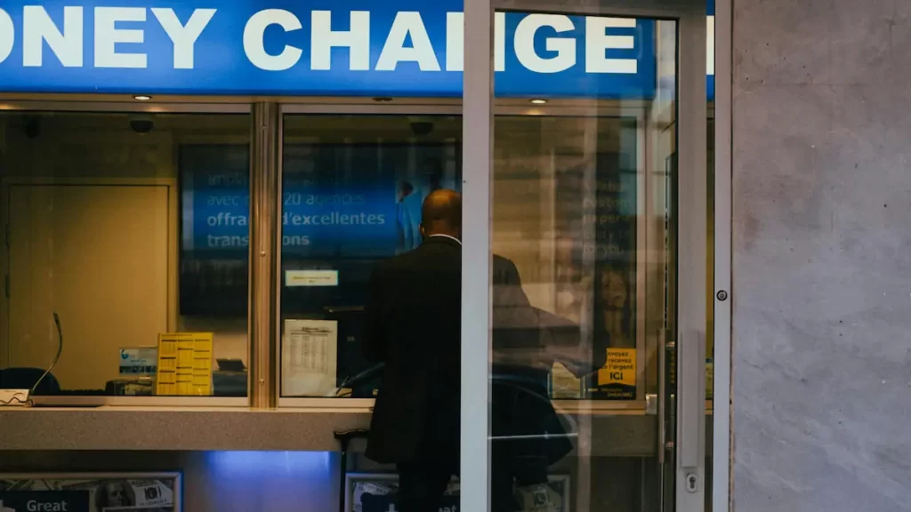 Man in a suit with his back to the camera stood in front of a counter with a sign above saying 'money change'.