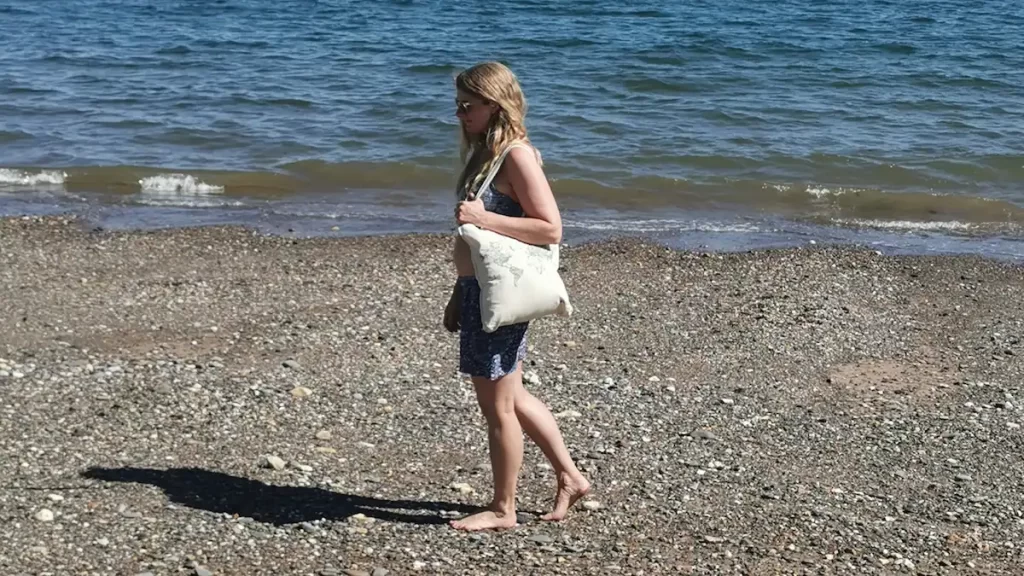 Woman walking along a beach carrying a white tote bag