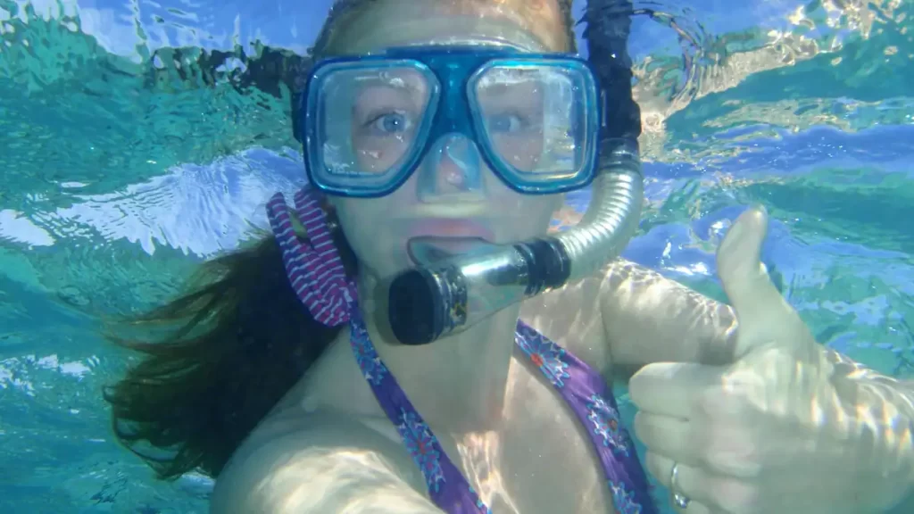 Woman underwater with snorkel on face taking a selfie doing a thumbs up pose to the camera
