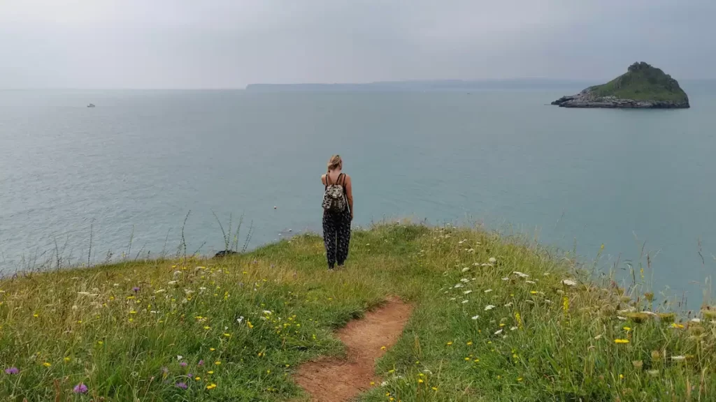 Woman stood on a grassy cliff looking out over the ocean