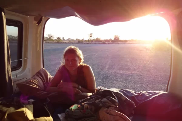 Sue (the founder of the Practical Passport) in the back of a campervan with a sunset behind her